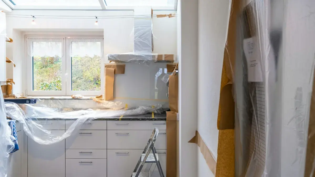 Kitchen under renovation with new white cabinets protected by plastic and paper