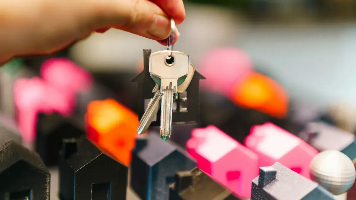 Hand holding a set of house keys above rows of miniature houses